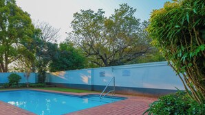 Una piscina con un vialetto in mattoni, circondata dal verde e da un muro bianco.