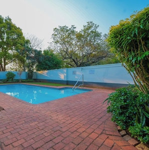 A swimming pool with a brick pathway, surrounded by greenery and a white wall. - Westridge Cozy Haven Fast WI-FI.Peace fully and comfortable (Berea)