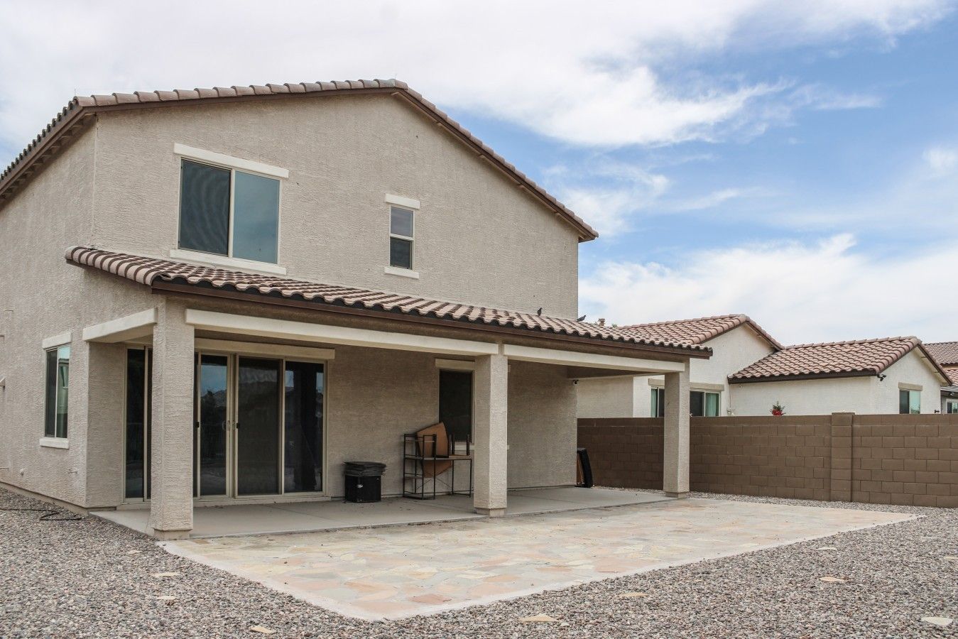 A two-story house with a covered patio, a fenced backyard, and a clear sky.
