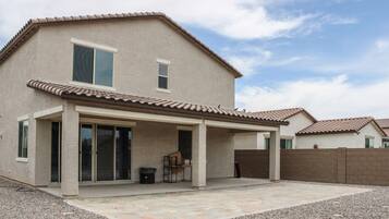 A two-story house with a covered patio, a fenced backyard, and a clear sky.