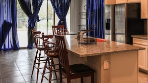 Een keuken met een granieten aanrecht, houten stoelen, een roestvrijstalen koelkast en blauwe gordijnen.