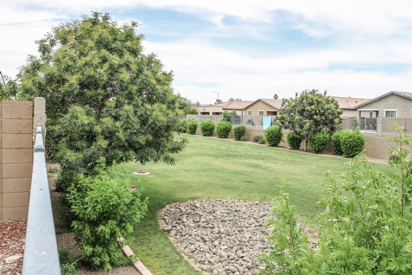 A residential area with a well-maintained lawn, a large tree, and multiple houses with similar architecture.