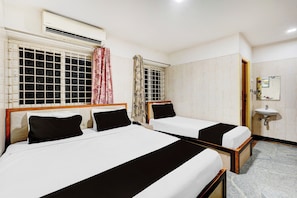 Hotellihuone, jossa on kaksi erillistä sänkyä, ikkuna, jossa on verho, yöpöytä ja seinälle asennettu pesuallas.