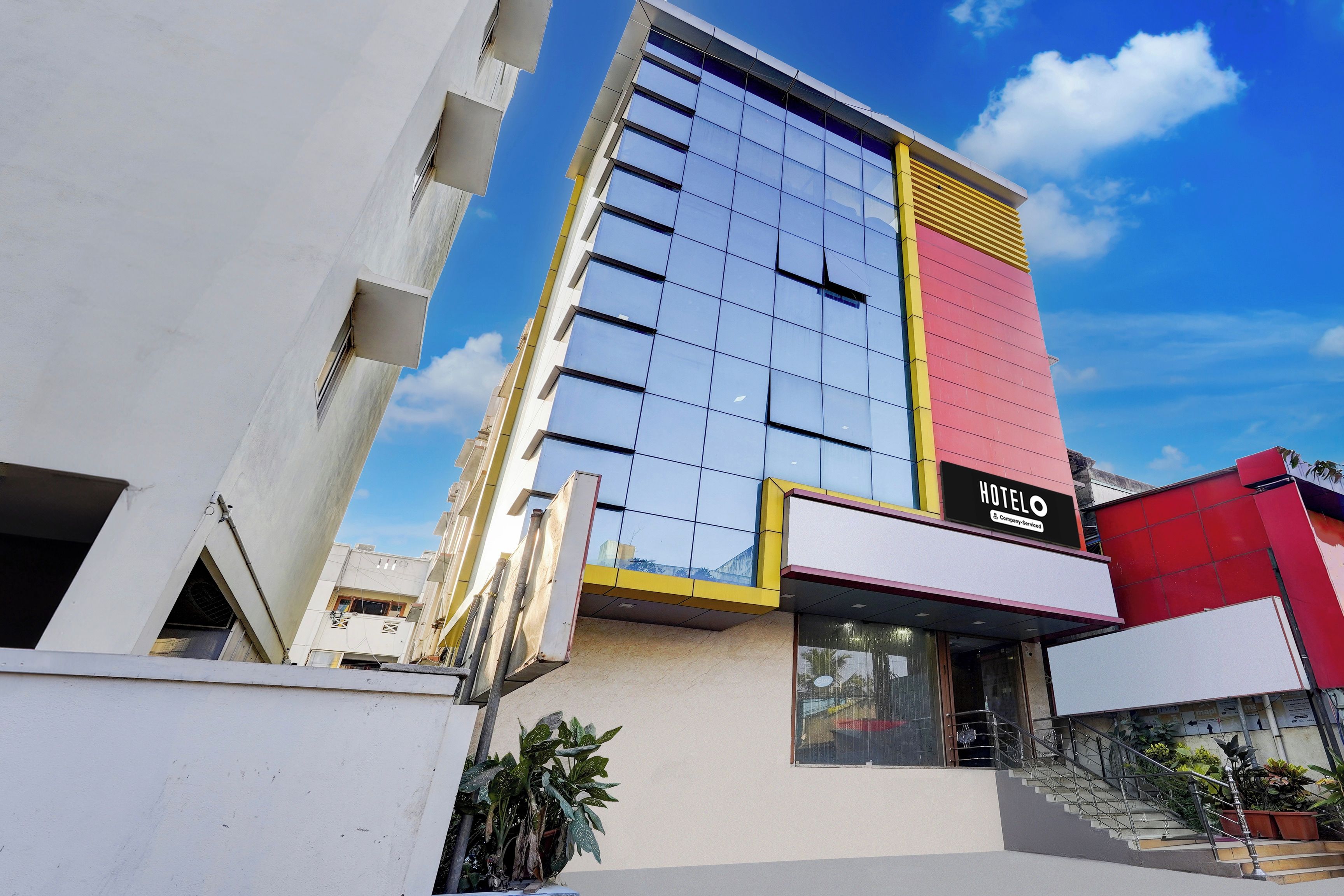A modern hotel building with a prominent 'HOTEL' sign, large windows, and a staircase leading to the entrance.