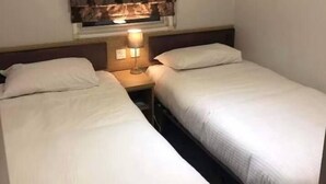 Hotellihuone, jossa on kaksi erillistä sänkyä, yöpöytä lampulla ja kukkakuviollinen verho.