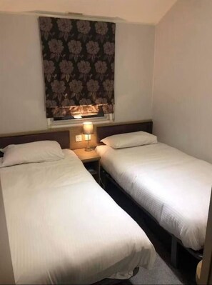 Ett hotellrum med två separata sängar, ett nattduksbord med en lampa och en gardin med blommönster.