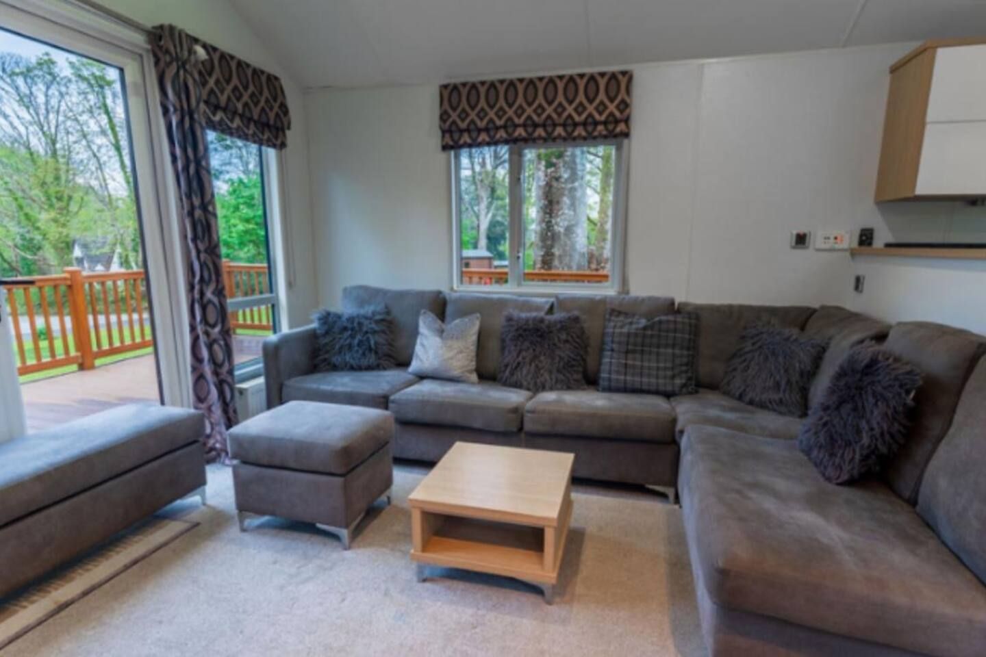 A living room with a grey sectional sofa, a wooden coffee table, and a patterned window valance.