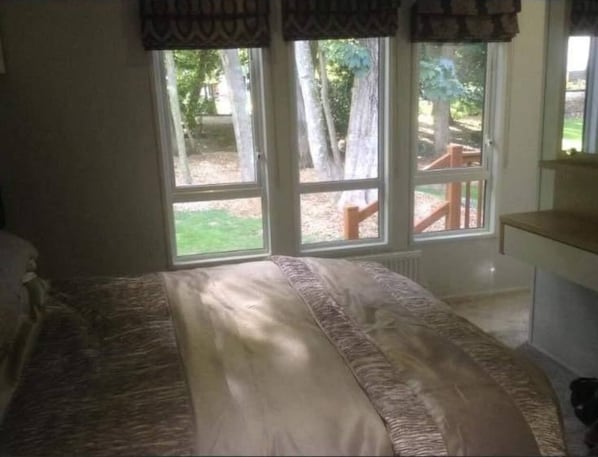 A bedroom with a large bed, two windows, and a view of the outdoors.
