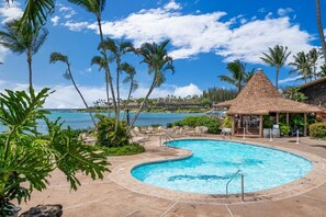Ein Swimmingpool mit einer strohgedeckten Struktur, umgeben von Palmen und Blick auf den Ozean.