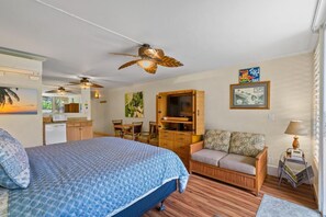 A hotel room with a bed, a sofa, a television, a ceiling fan, and a bar area. - Napili Shores #d-128 1 Bedroom Condo (Lahaina)