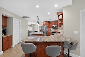 A kitchen with granite countertops, wooden cabinets, a stainless steel refrigerator, and a microwave. - Lakeland 4br Vacation Home Sleeps 9 Pool 4 Bedroom Home (Lakeland)
