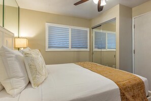 A bedroom with a bed, a nightstand, a lamp, a window with blinds, and a wardrobe. - Maalaea Kai #220 2 Bedroom Condo (Wailuku)