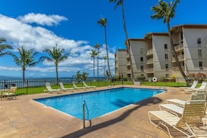 A swimming pool with lounge chairs, palm trees, and a view of the ocean. - Maalaea Kai #220 2 Bedroom Condo (Wailuku)