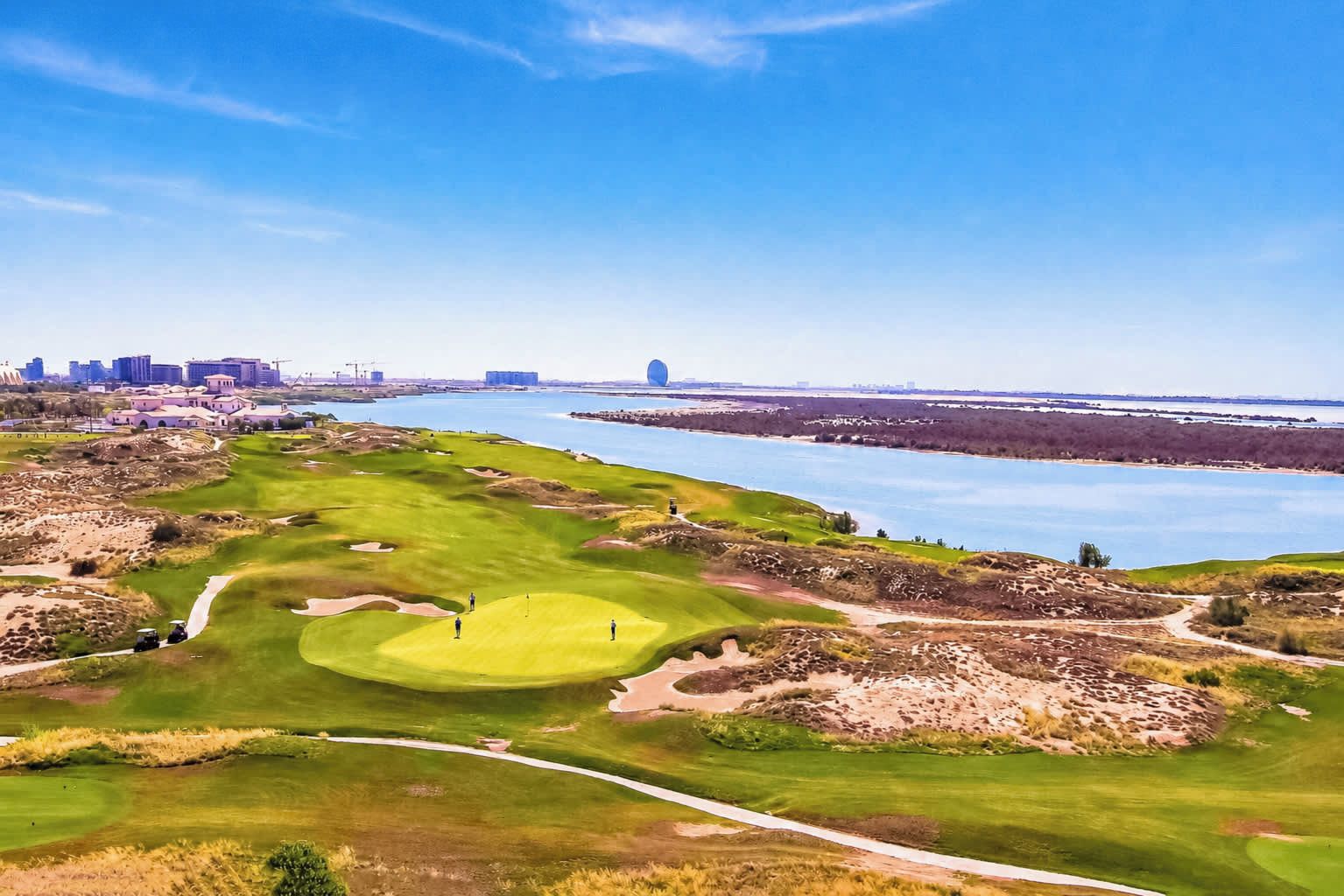 A golf course with a water body in the background and a city skyline.