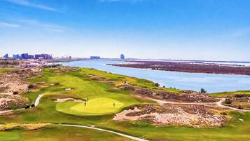 A golf course with a water body in the background and a city skyline.