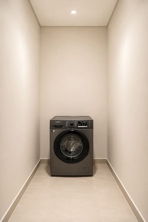 Een compacte, moderne wasmachine in een smalle gang met een effen muur en een inbouwspots.