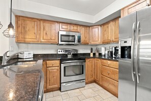 A modern kitchen with wooden cabinets, stainless steel appliances, a granite countertop, and a built-in oven. - MP326 Mountain Plaza 2 Bedroom 3 Bath 2 Condo (Copper Mountain)