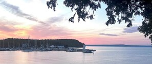 A marina with boats docked, a lighthouse, and a forested hill in the background. - Lighthouse Lodge-Lion's Head, Tobermory, The Grotto, Flowerpot, Bruce Trail (Lion's Head)