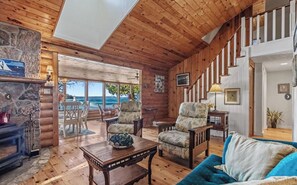 A log cabin interior with a stone fireplace, wooden furniture, and a view of the ocean. - Lighthouse Lodge-Lion's Head, Tobermory, The Grotto, Flowerpot, Bruce Trail (Lion's Head)
