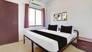 A bedroom with a bed, a wardrobe, an air conditioning unit, a window with curtains, and wall art. - Hotel O Rane Nagar (Nashik)