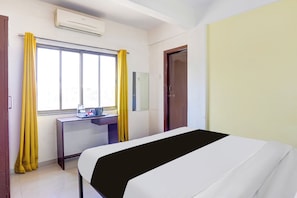 A hotel room with a bed, a desk, a window with curtains, an air conditioning unit, and a door. - Hotel O Rane Nagar (Nashik)