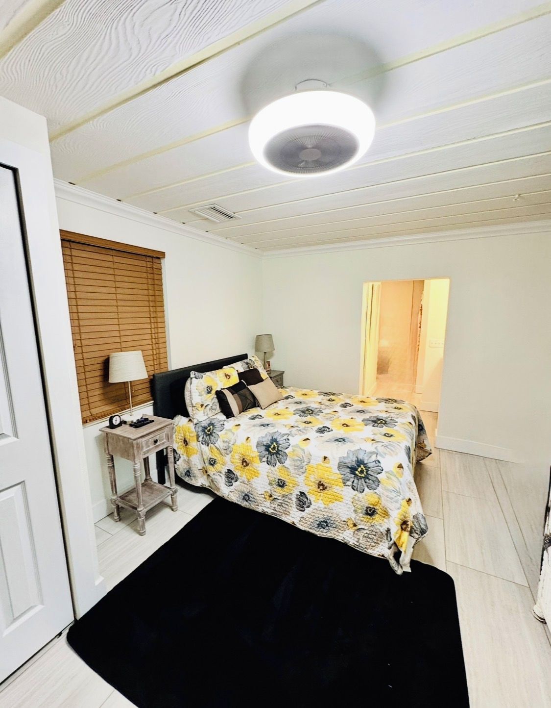 A bedroom with a bed, a bedside table, a lamp, a ceiling light, and a door.