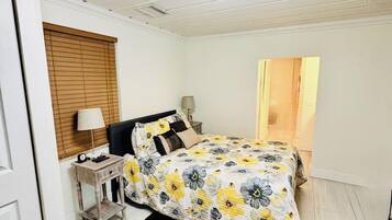 A bedroom with a bed, a bedside table, a lamp, a ceiling light, and a door.
