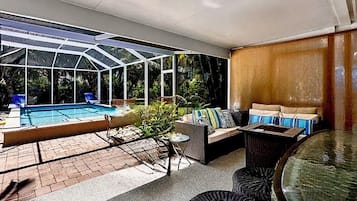 A covered outdoor area with a pool, seating, and a glass enclosure.