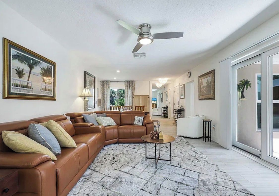 A spacious living room with a brown leather sofa, a round coffee table, and a ceiling fan.