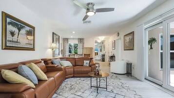 A spacious living room with a brown leather sofa, a round coffee table, and a ceiling fan.