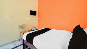 Hotellihuone, jossa on sänky, tuoli, pieni pöytä ja vedenkeitin sekä seinälle asennettu taulutelevisio.