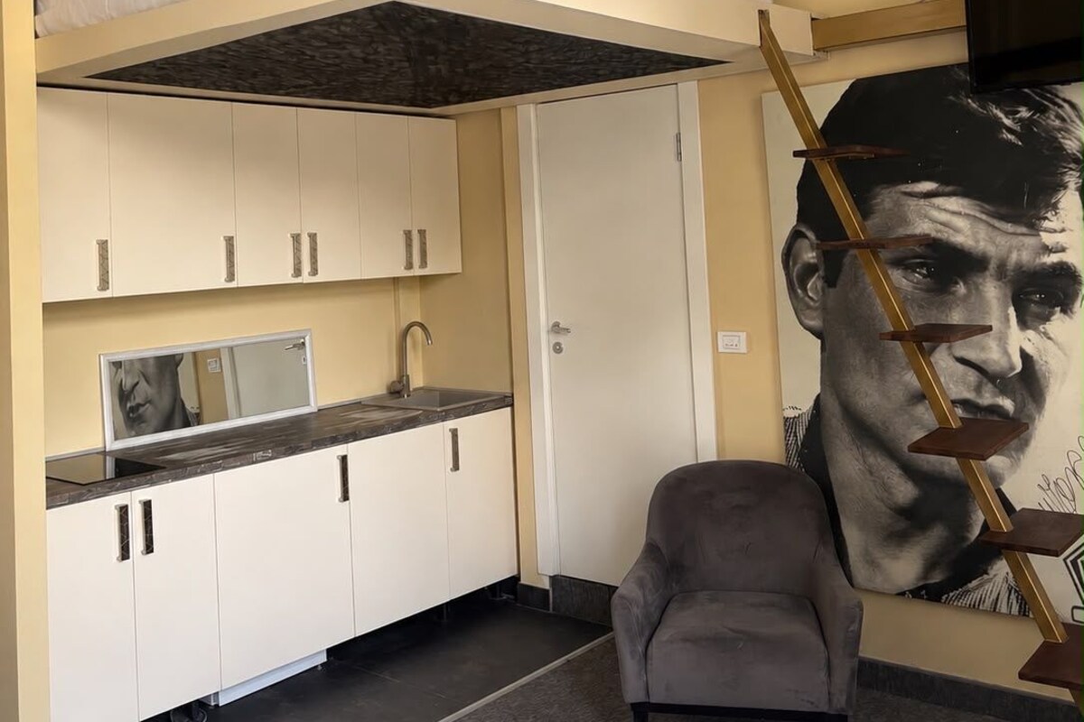 Ein kleines Zimmer mit Etagenbett, Küchenzeile und einem großen Plakat.