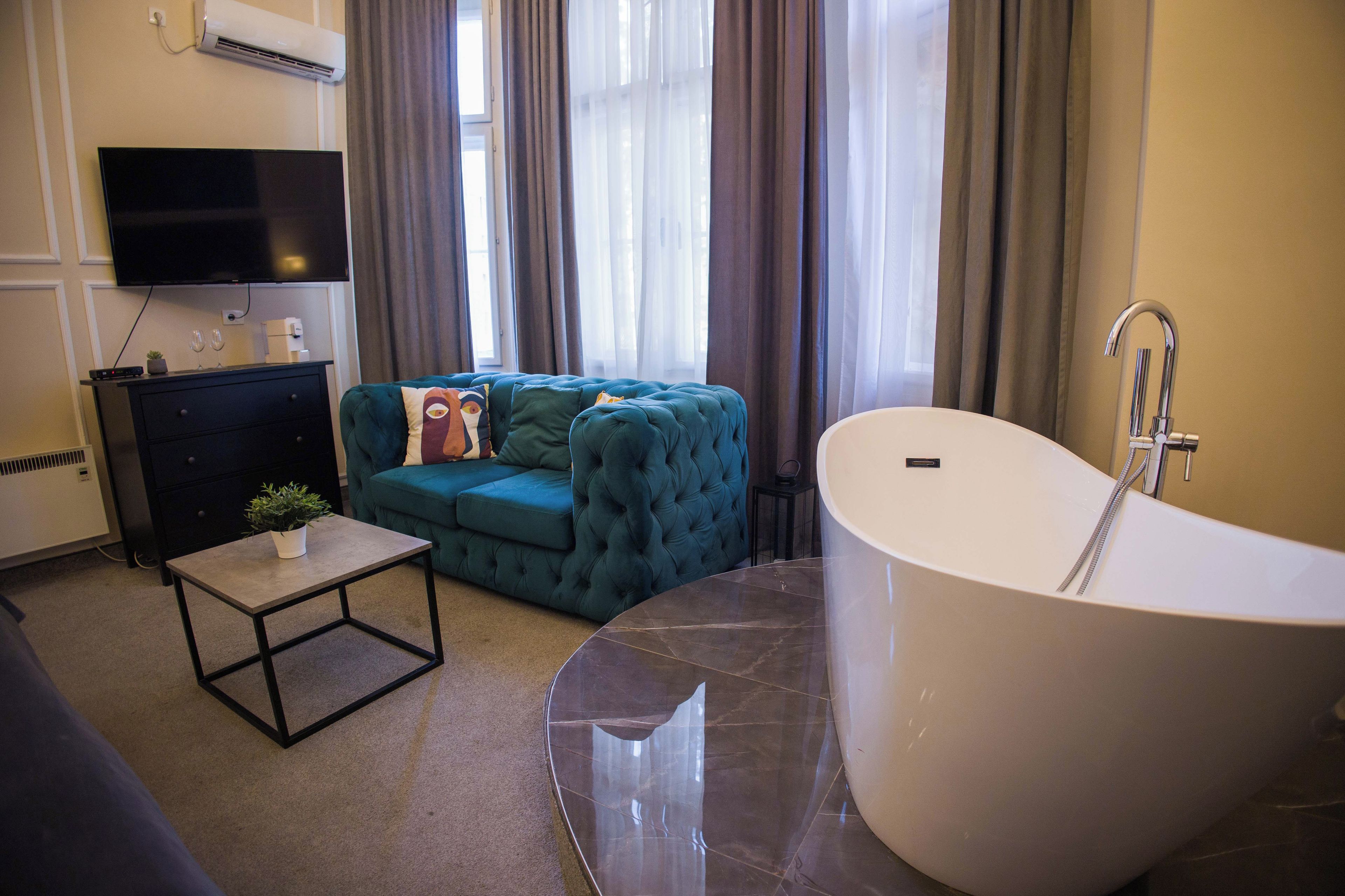 Une salle de bain moderne avec une baignoire sur pieds, un canapé, une petite table avec une plante et un téléviseur à écran plat fixé au mur.