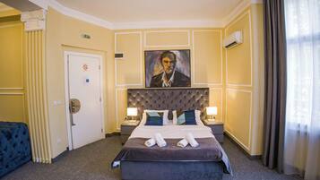 A hotel room with a large bed, two bedside tables with lamps, a painting on the wall, and a door with an exit sign.