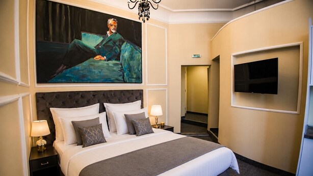 Een hotelkamer met een groot bed, een schilderij erboven, een flatscreen televisie aan de muur en een vluchtroute aanduiding.