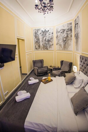 Ein Hotelzimmer mit einem Bett, zwei Sesseln, einem Fernseher und Kunstwerken an den Wänden.