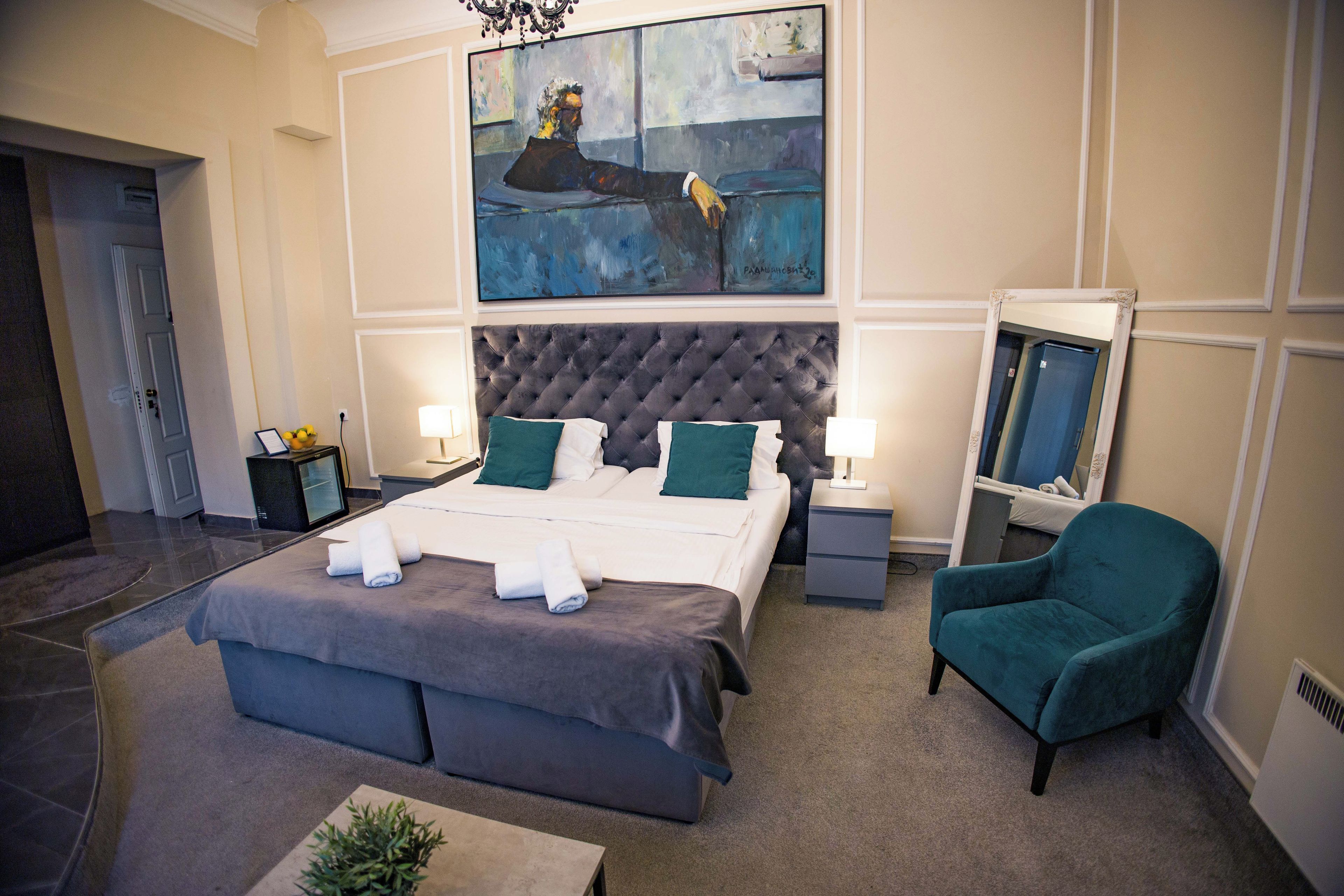 A hotel room with a large bed, two bedside tables, a chair, a painting, and a mirror.