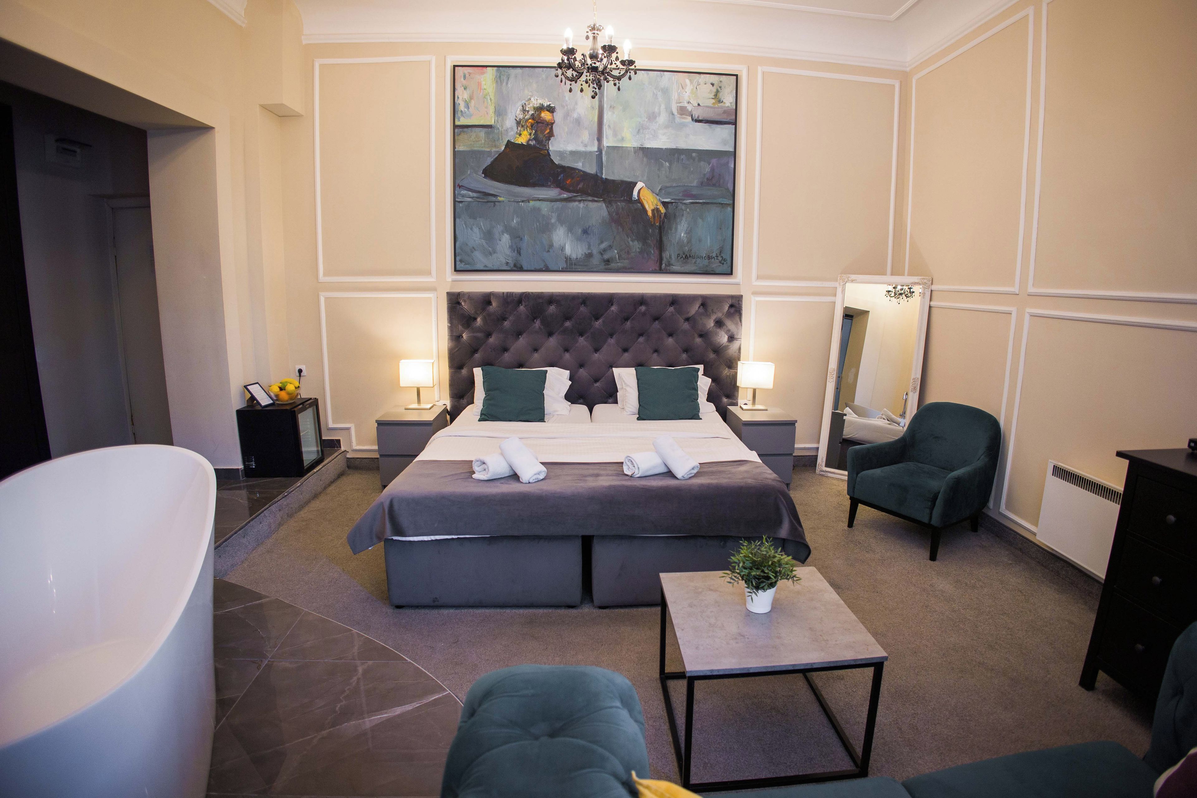 Een moderne hotelkamer met een groot bed, een zithoek met een fauteuil, een klein tafeltje en een groot schilderij aan de muur.