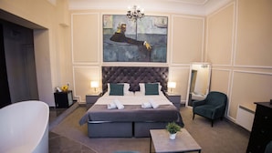 Een moderne hotelkamer met een groot bed, een zithoek met een fauteuil, een klein tafeltje en een groot schilderij aan de muur.