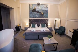Ein modernes Hotelzimmer mit einem großen Bett, einer Sitzecke mit einem Sessel, einem kleinen Tisch und einem großen Gemälde an der Wand.