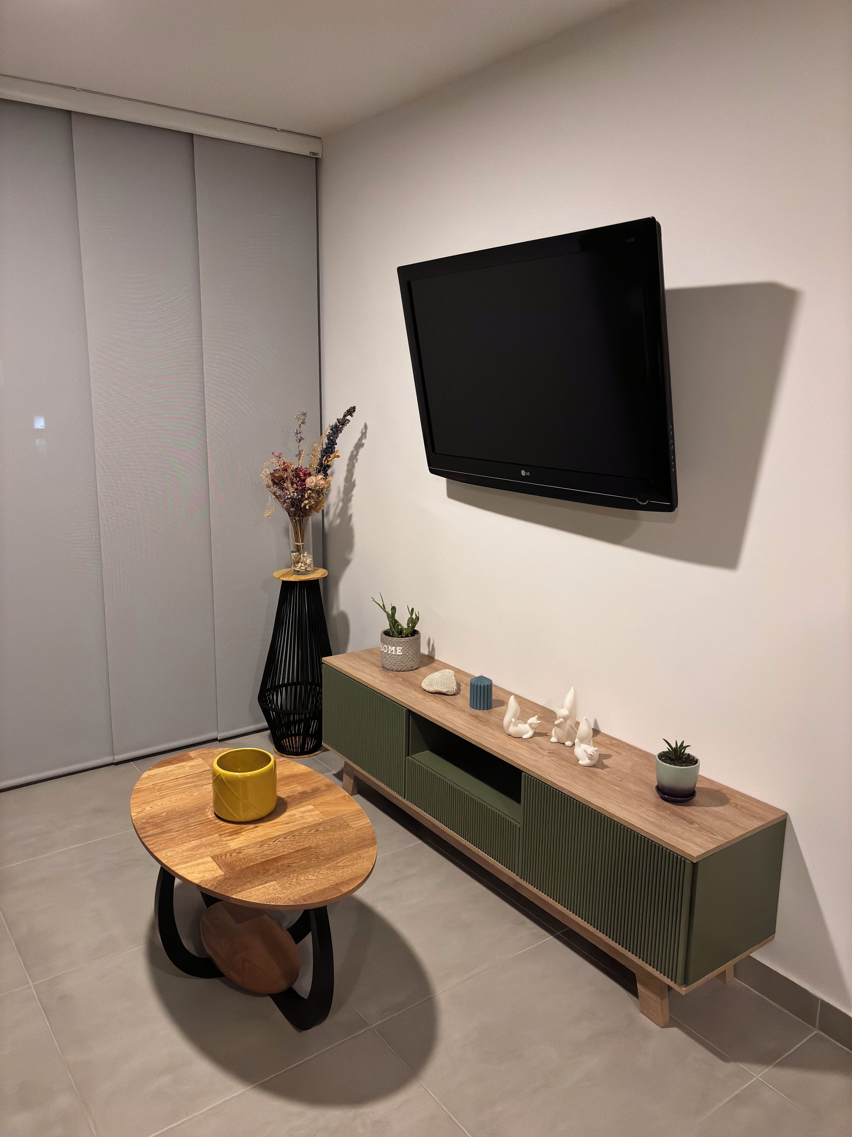 Un saló modern amb una televisió de pantalla plana penjada a la paret, una taula de centre de fusta i una consola verda amb objectes decoratius.