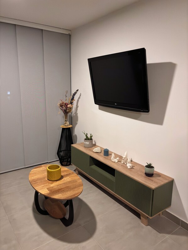 Una sala moderna con un televisor de pantalla plana montado en la pared, una mesa de centro de madera y un mueble consola verde con objetos decorativos.