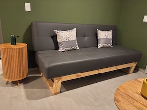 A modern room with a grey sofa, two patterned pillows, a wooden side table, and a round wooden table. - Charming Apartment in Piedra Pintada | 2 Bedrooms, Pool & Mountain Views (Ibagué)