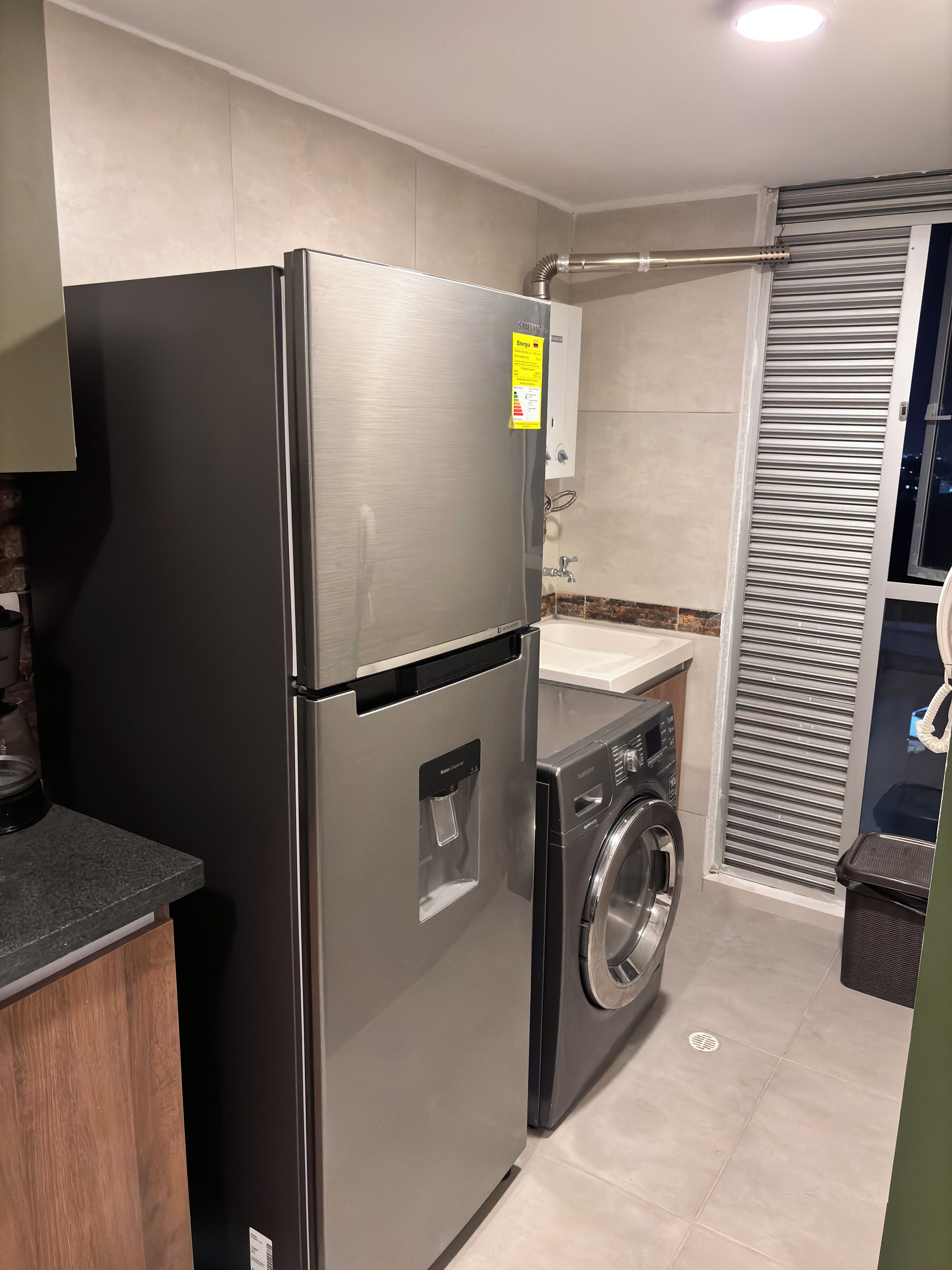A compact kitchen with a stainless steel refrigerator, a built-in washing machine, and a small countertop.