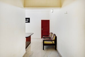 A hallway with a red door, a bench, and a sign indicating a service area. - Hotel O Kilpauk Near Don Bosco College (Chennai)