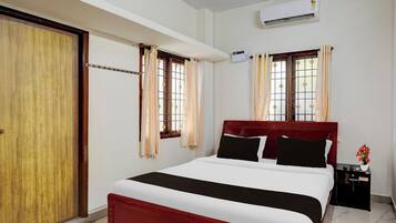 A hotel room with a bed, a wardrobe, a nightstand, and an air conditioning unit.