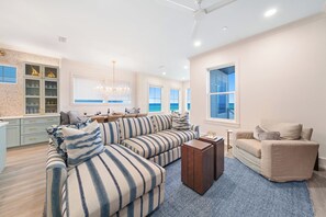 Ein geräumiges Wohnzimmer mit einer großen Eckcouch, einer kleinen Couch und einem Couchtisch. Mehrere Fenster bieten Blick auf den Ozean.