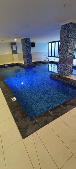 An indoor swimming pool with tiled walls and a tiled floor. - Perth City 2BR Apartment | Pool & Parking (East Perth)