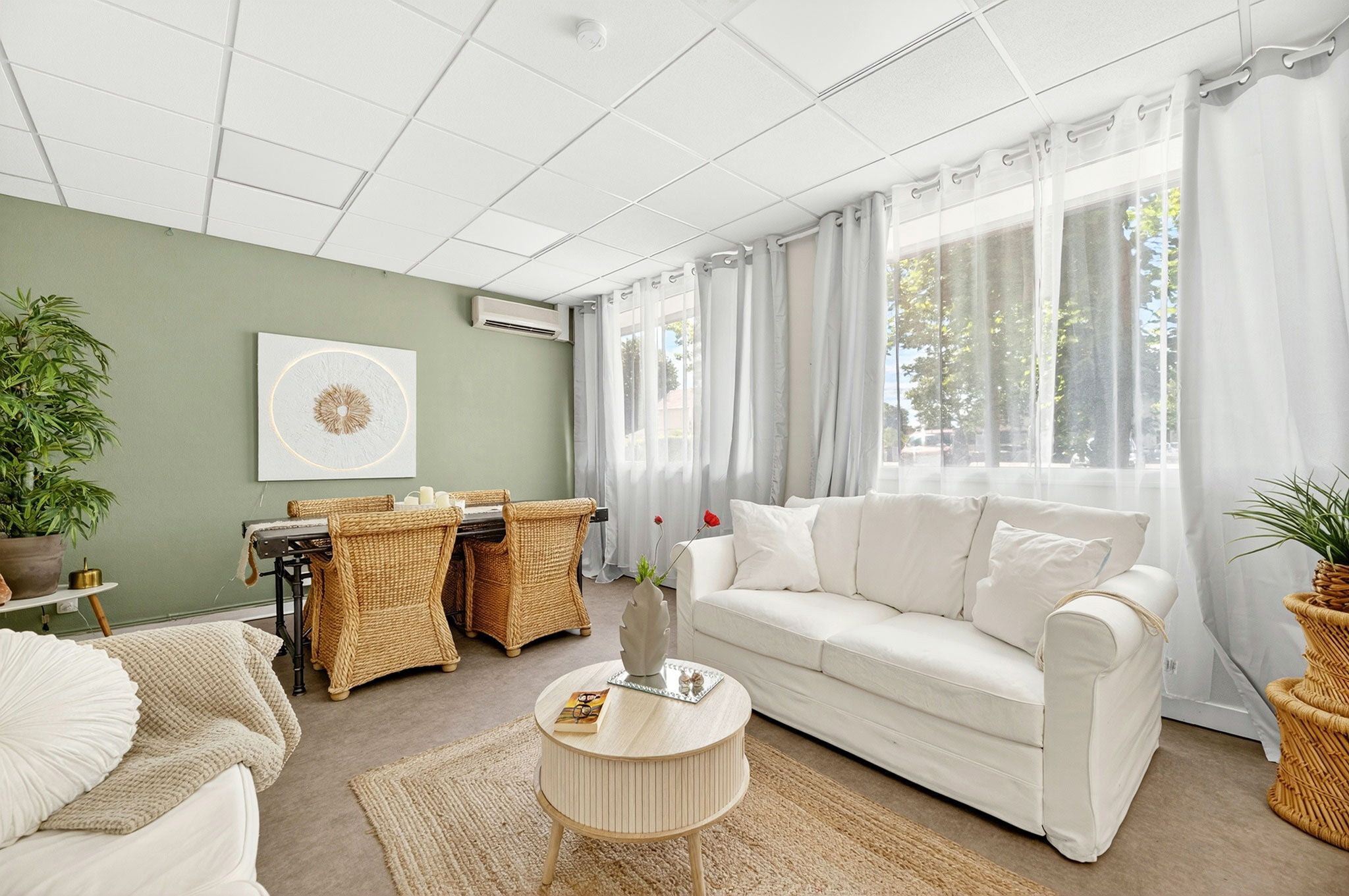 A living room with a white sofa, wicker chairs, a round coffee table, and a dining area with a table and chairs.
