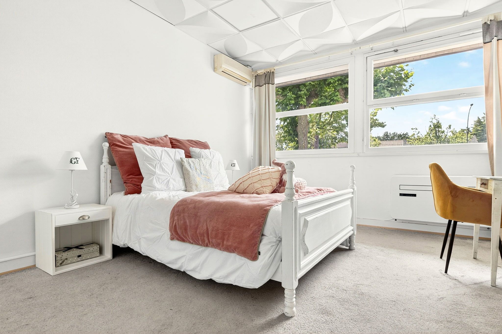 A bedroom with a bed, bedside table, lamp, and a desk with a chair.